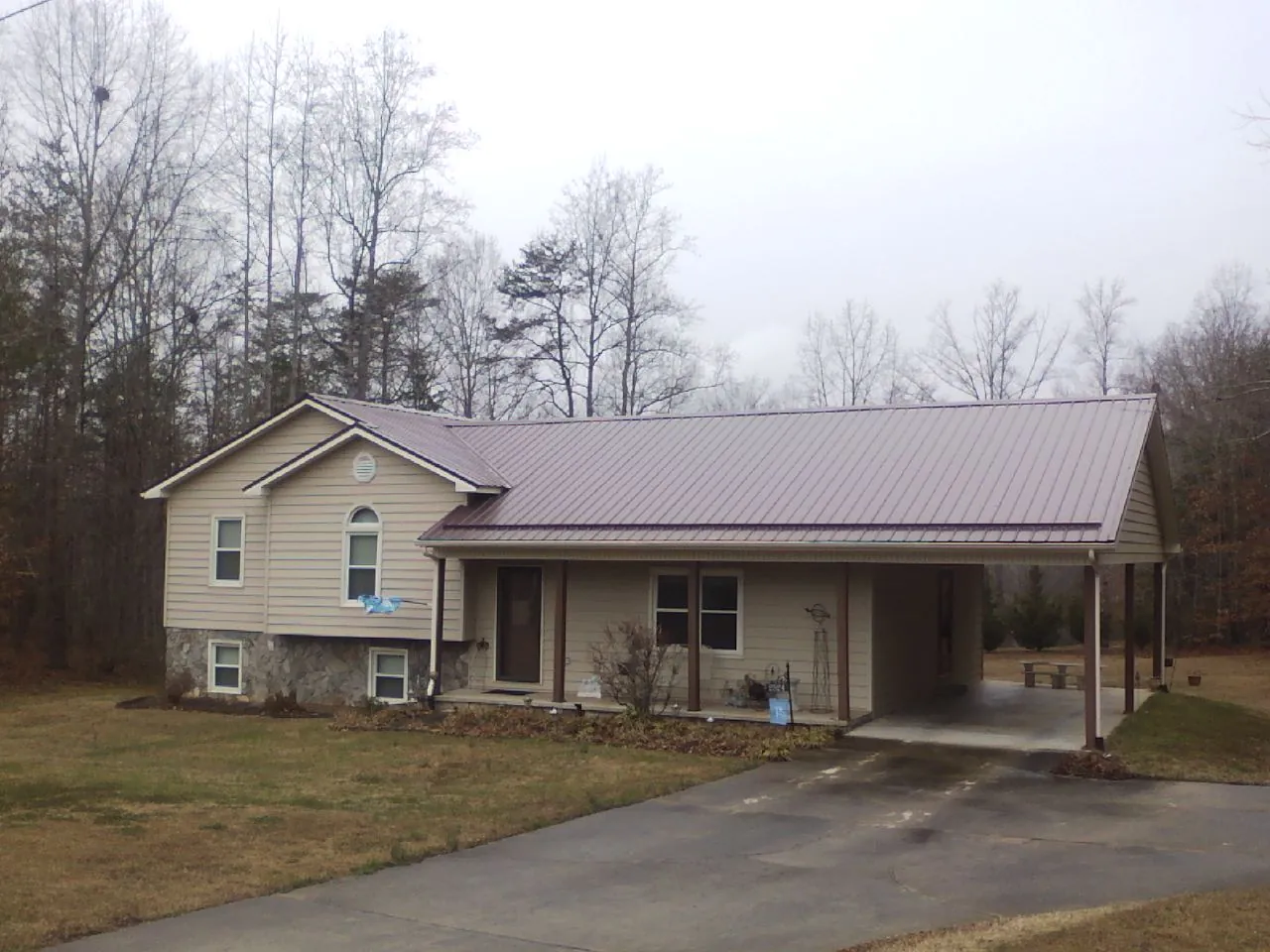 Burgundy metal roof on a tan split level home with an attached carport in Kingston